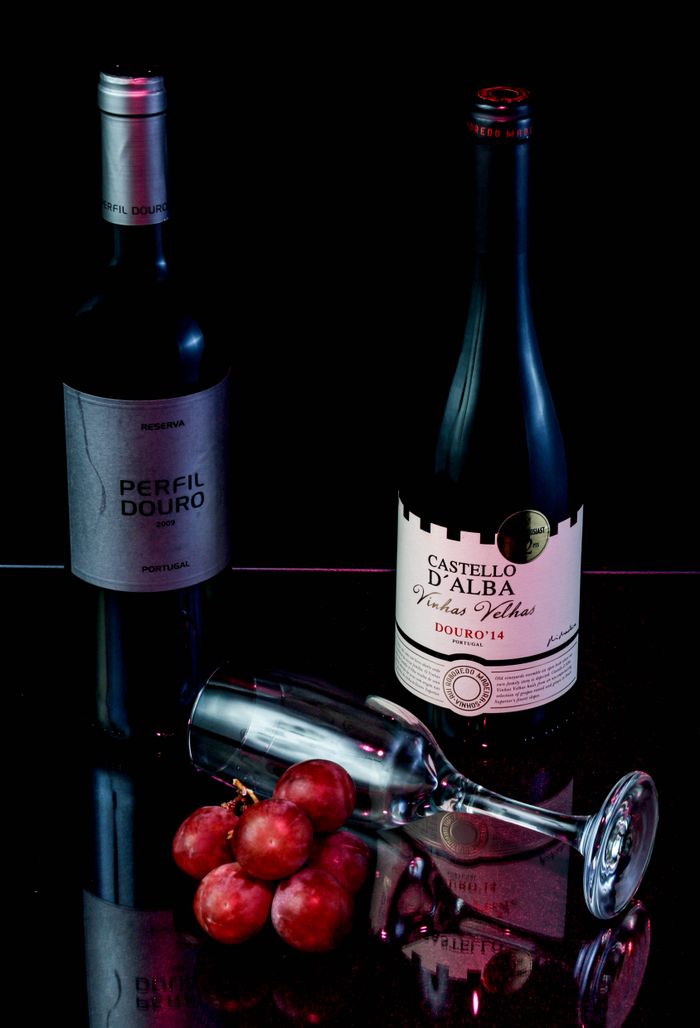about-me Two red wine bottles with grapes and a glass on a reflective surface.